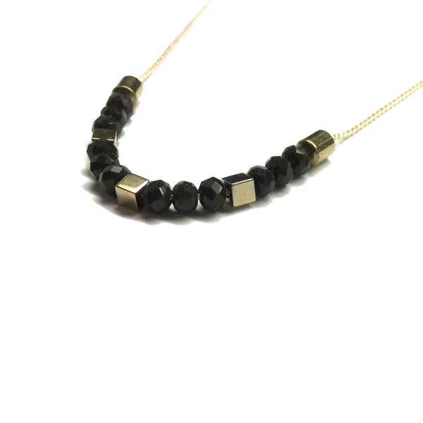 Gold brass tube bead with black faceted glass beads and gold square hematite bead spacers on a thread necklace